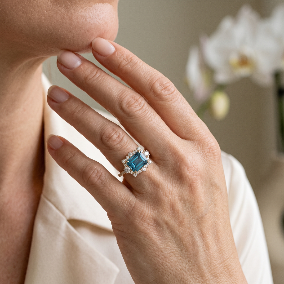 Emerald-cut blue moissanite halo ring in rose gold worn on a woman's hand.