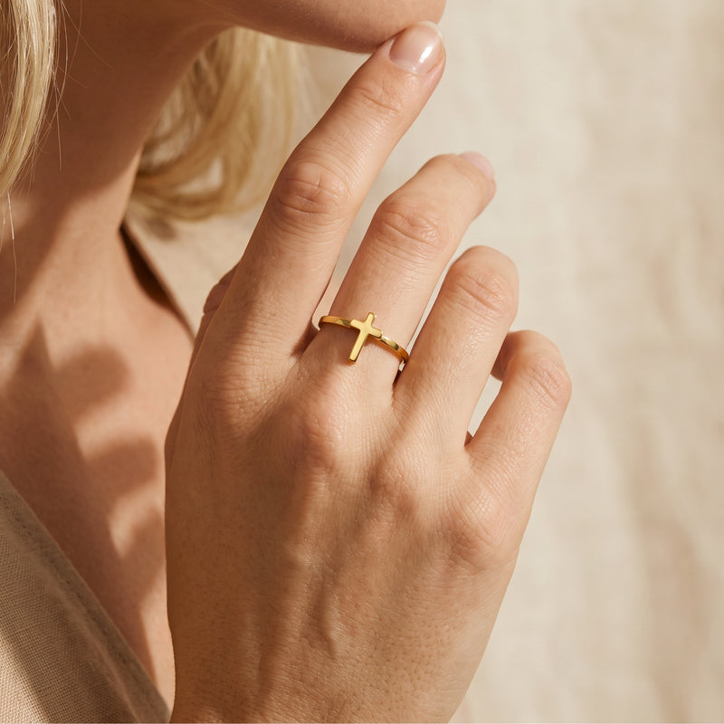 Close-up of a hand wearing the gold-tone open cross ring on the middle finger.