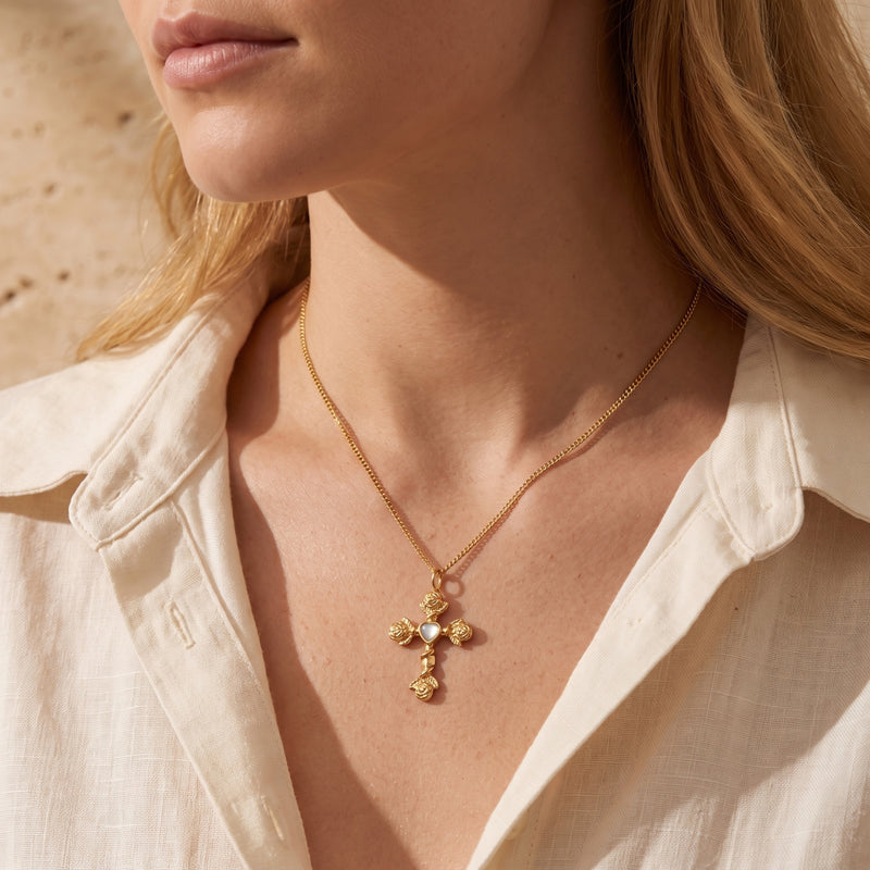 Close-up of a model wearing the gold-tone rose cross necklace with a heart center and an open beige shirt.