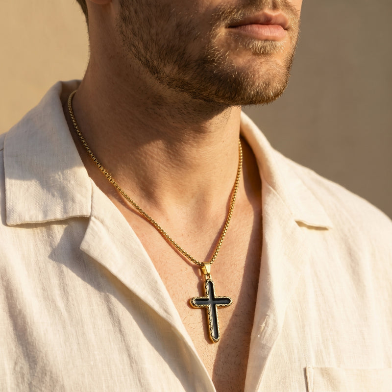 Model wearing a gold-tone black-inlay cross necklace on a box chain with an open white shirt.