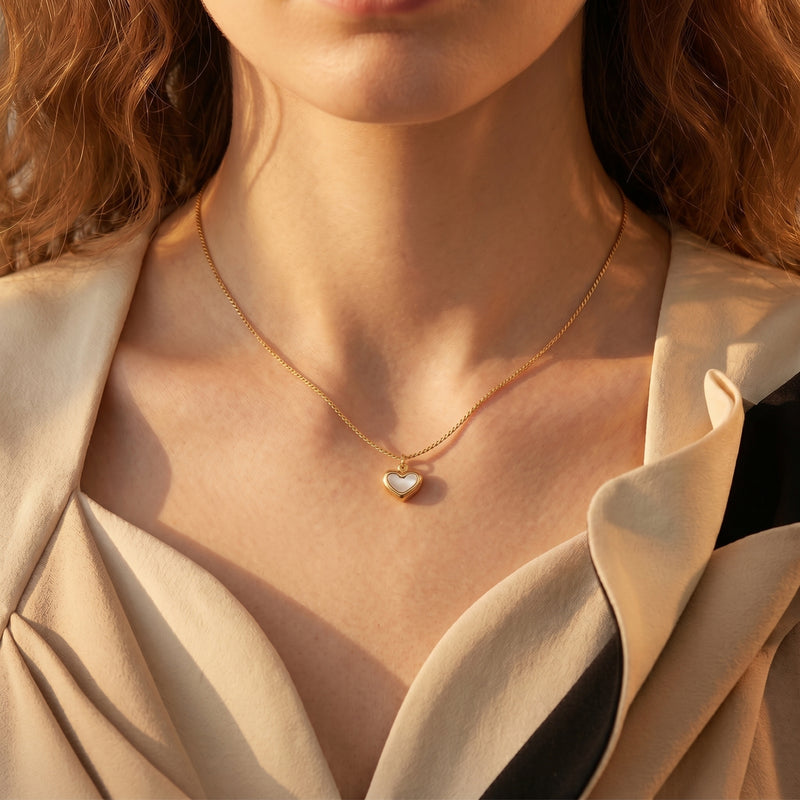 Gold heart pendant necklace with white inlay worn by a model against a neutral top.