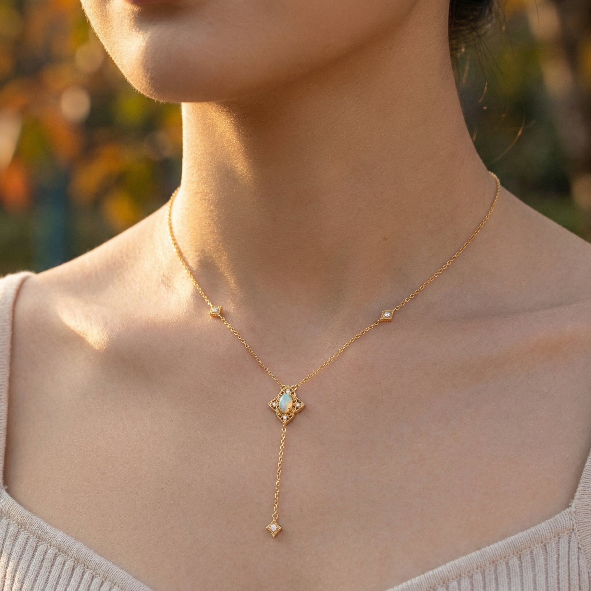 Gold-tone lariat necklace with a white opal oval drop pendant worn by a model.