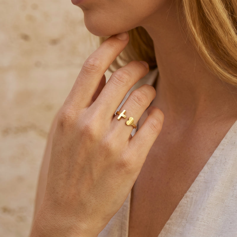 Close-up of a woman wearing the gold-tone heart and cross open ring on her ring finger near her face.