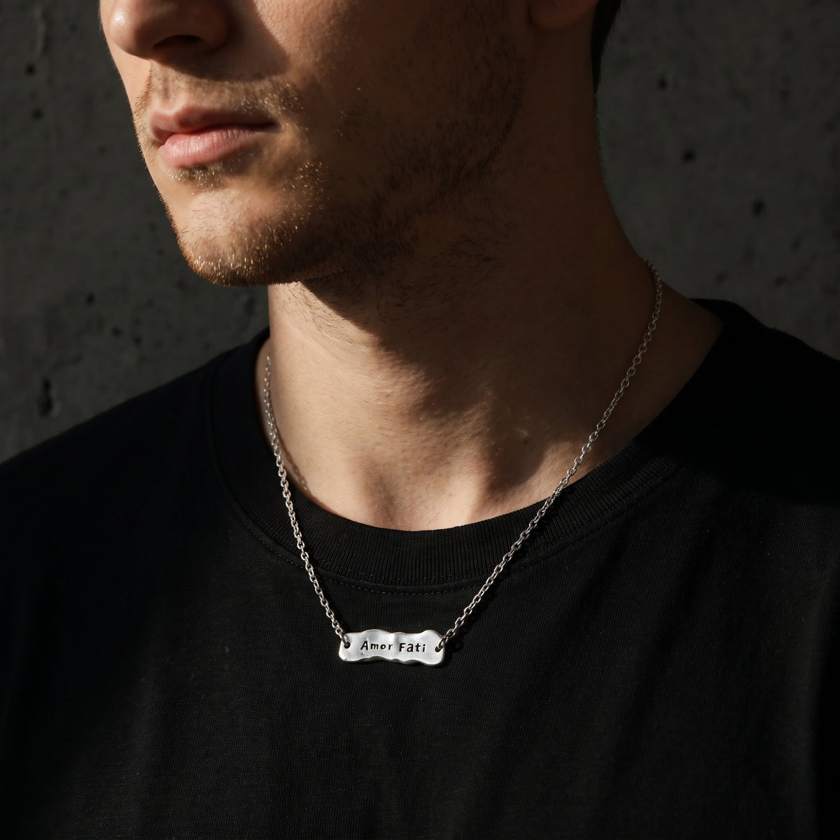 Close-up of a man wearing the silver Amor Fati bar necklace over a black T-shirt.
