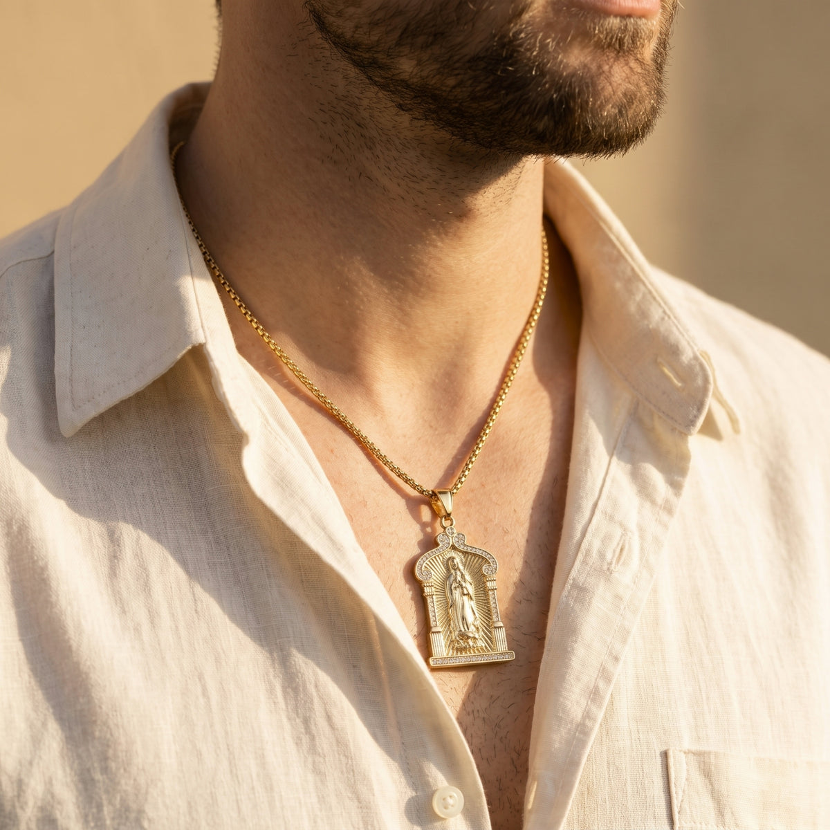 Close-up of a man wearing the gold-tone Guadalupe arch pendant on a box chain over an open white shirt.