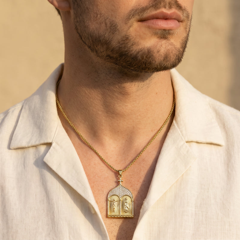 Front view of a man wearing the gold-tone diptych pendant necklace over an open white shirt.