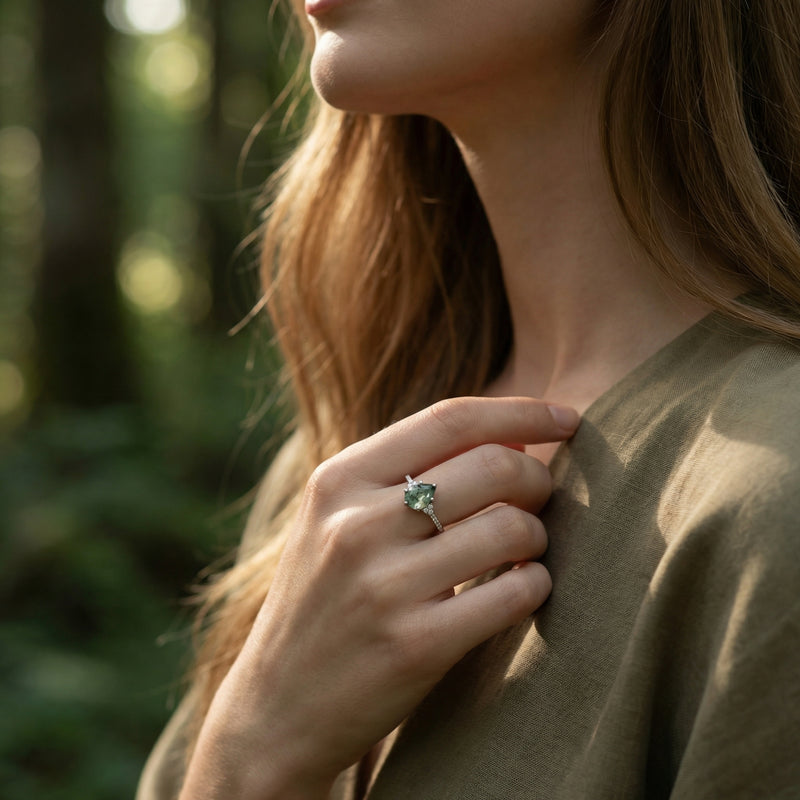 Model wearing a pear cut moss agate sterling silver ring on her finger in a sunlit forest setting.