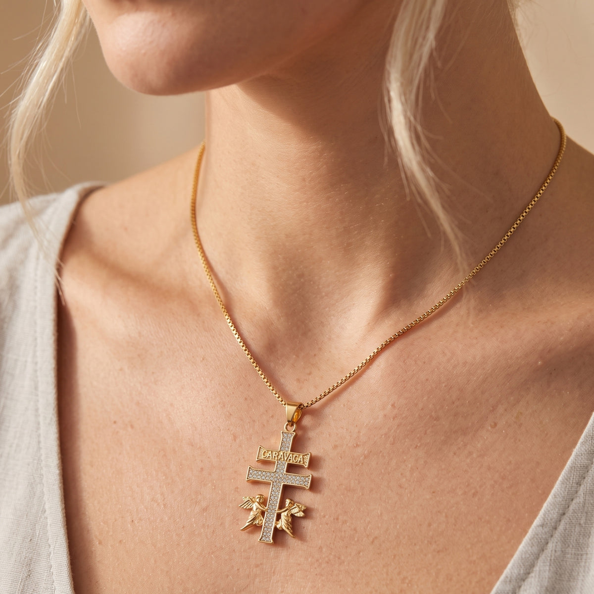 Gold Caravaca cross pendant necklace worn around a woman's neck.