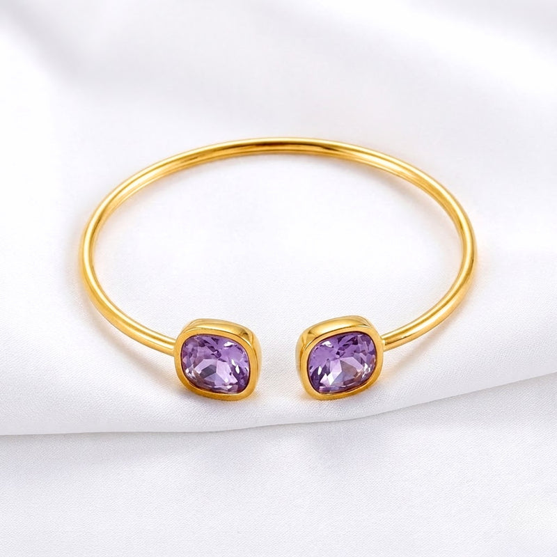 Front view of the gold Aurelia bangle with two cushion-cut simulated amethyst stones on white fabric.