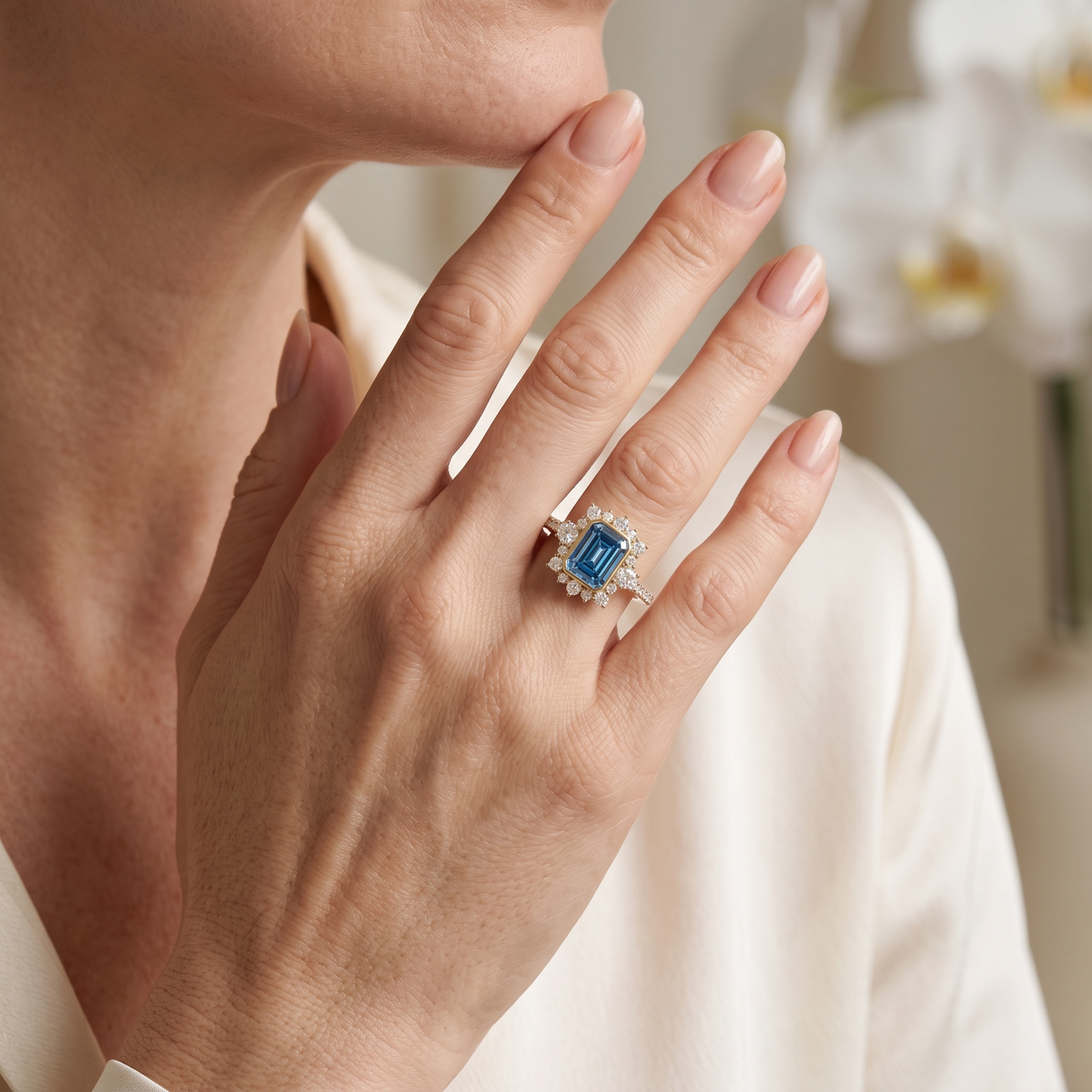 Emerald-cut blue gemstone halo ring in rose gold worn on a woman's hand.