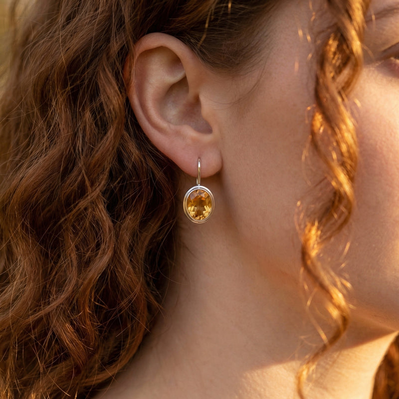 Model wearing a sterling silver drop earring featuring a faceted oval natural citrine gemstone.