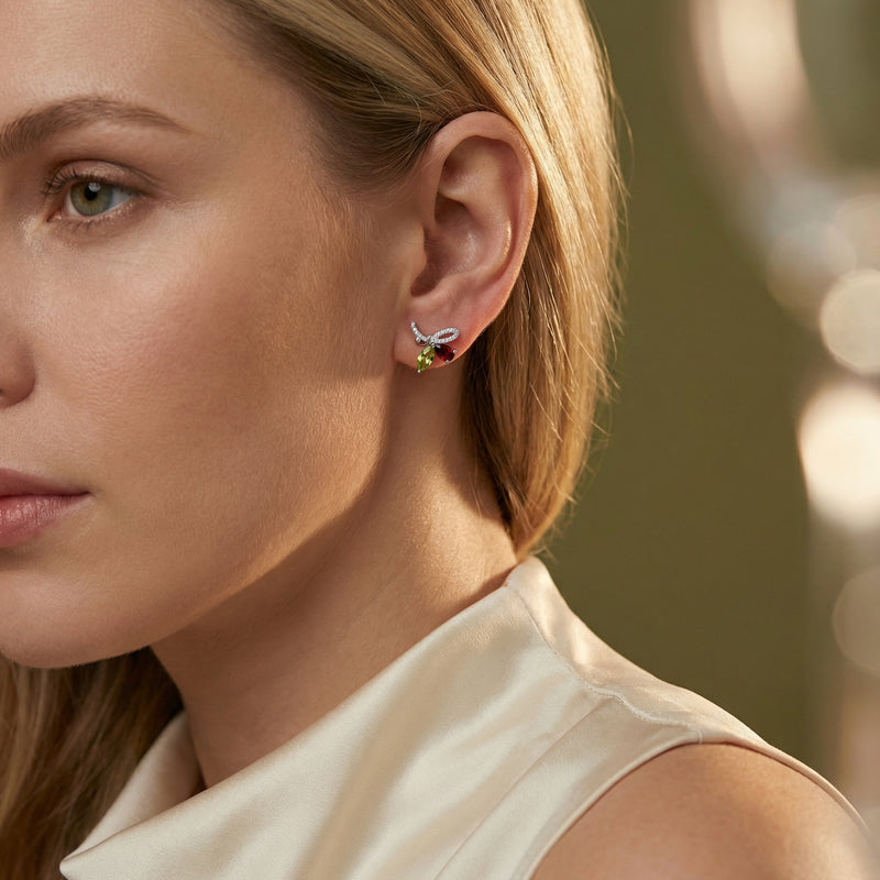 Model wearing the Giselle Marquise sterling silver bow earrings featuring marquise-cut peridot and red gemstones.