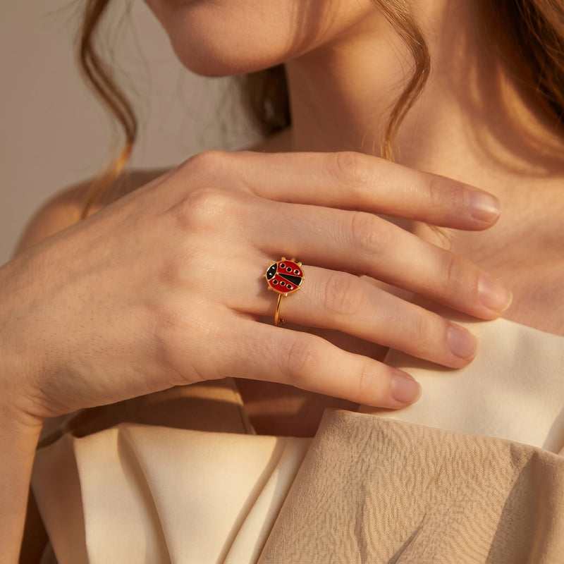 Gold finish ladybug ring with red and black enamel worn on a woman's finger.
