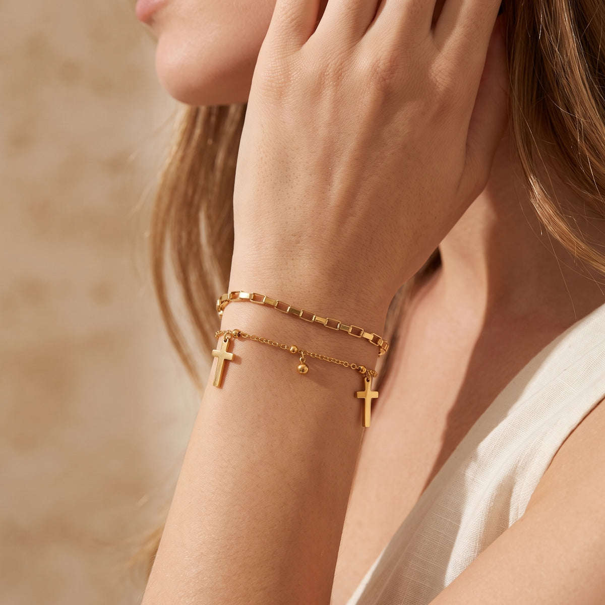 Close-up of a woman wearing the gold-tone double-layered cross bracelet with her wrist raised near her jaw.