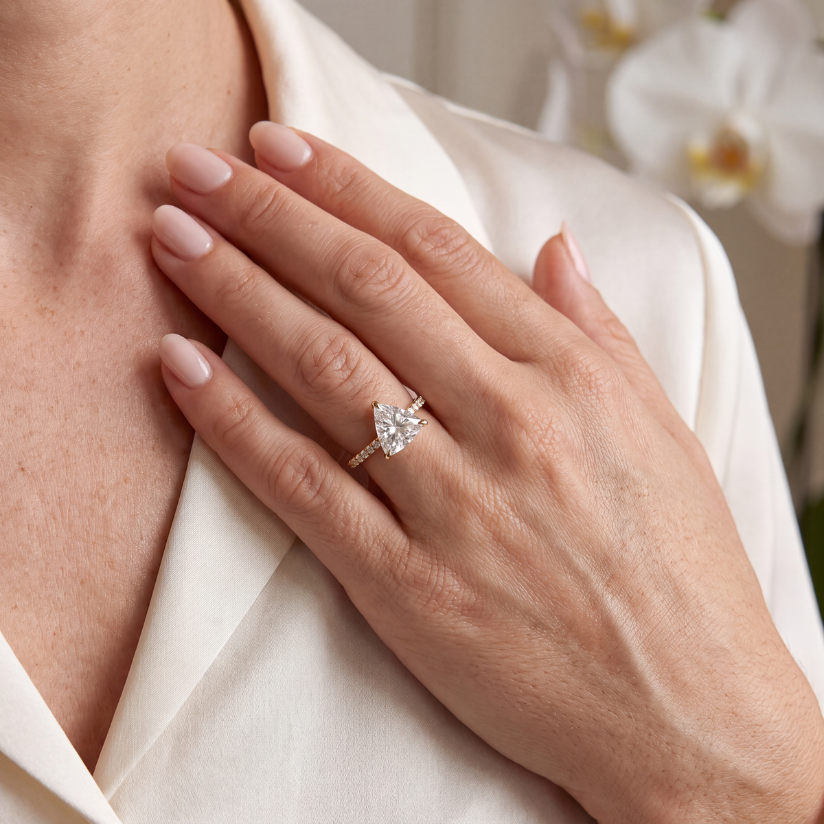 A model wearing a yellow gold trillion-cut moissanite engagement ring on her ring finger.