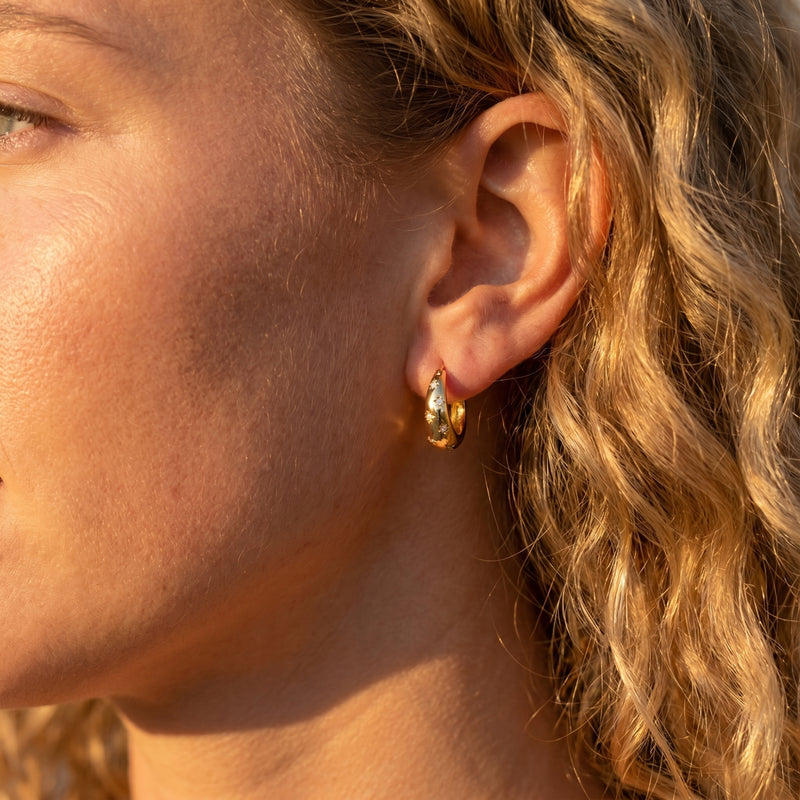 Gold Stellaura starburst huggie hoop earring with diamond accents worn on a woman's ear.