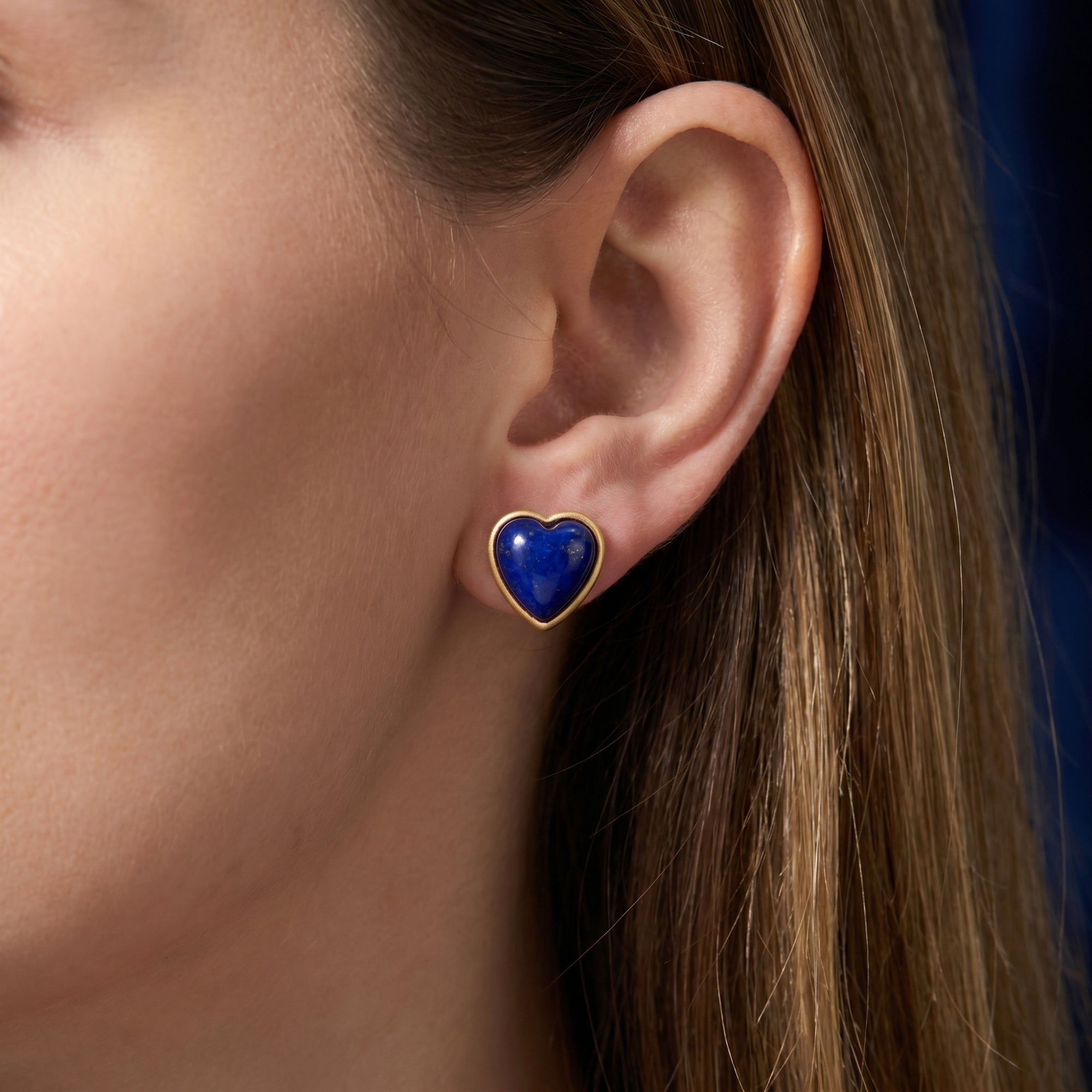 Model wearing a heart-shaped natural lapis lazuli cabochon stud earring in 18k gold plating.