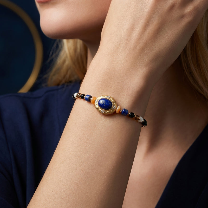 Gold-plated lapis lazuli bead bracelet worn on a woman's wrist, featuring a central oval lapis cabochon.