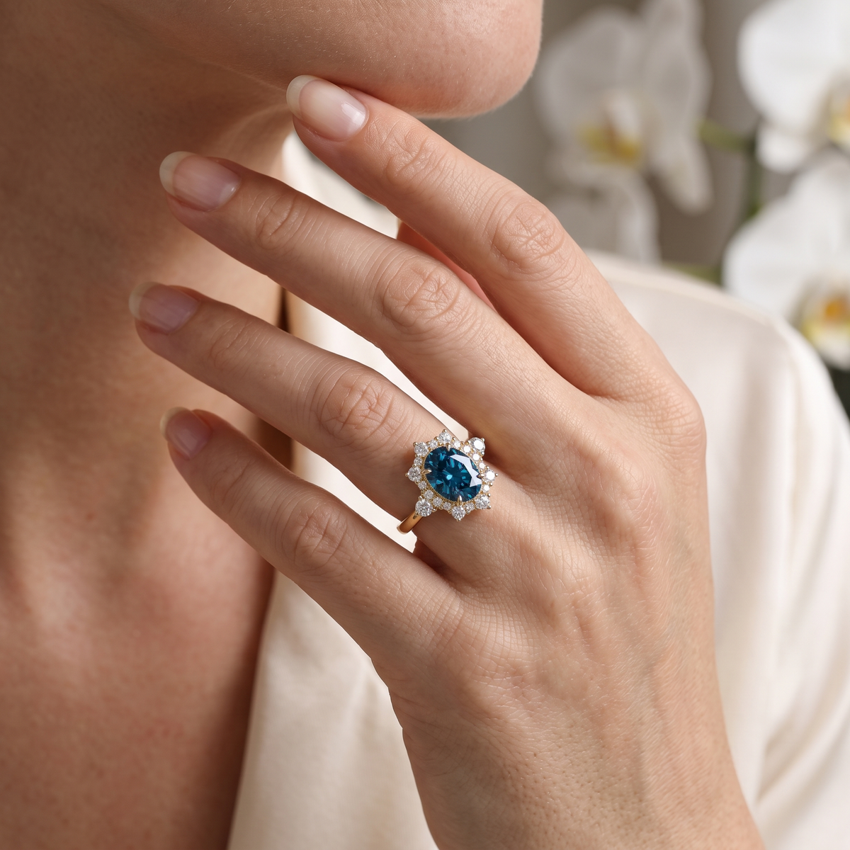 Close-up of a hand wearing a vintage-inspired rose gold halo ring with an oval blue moissanite gemstone.