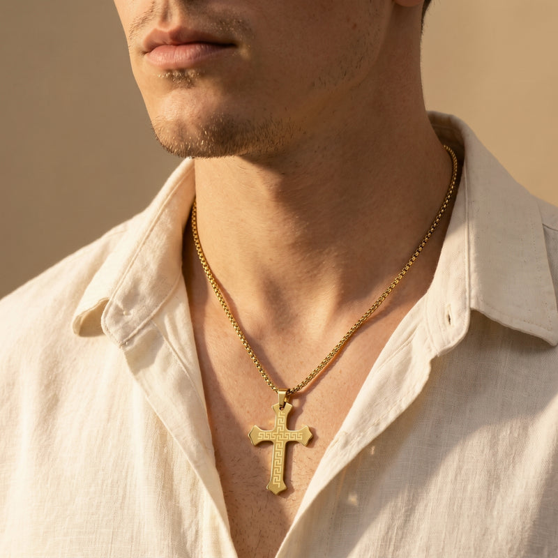Model wearing the gold-toned Greek key cross necklace over an open white shirt.