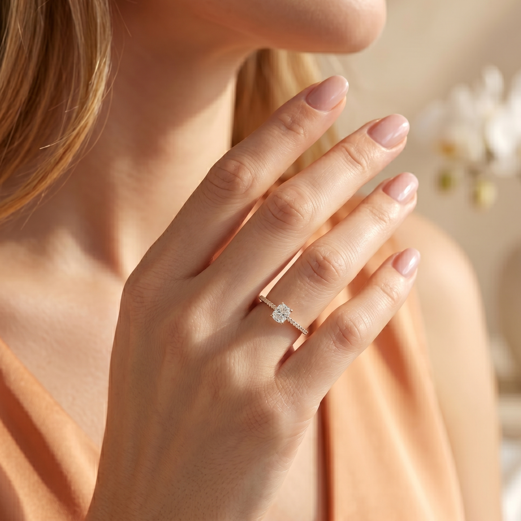 A delicate cushion-cut moissanite engagement ring in yellow gold worn on a model's hand.