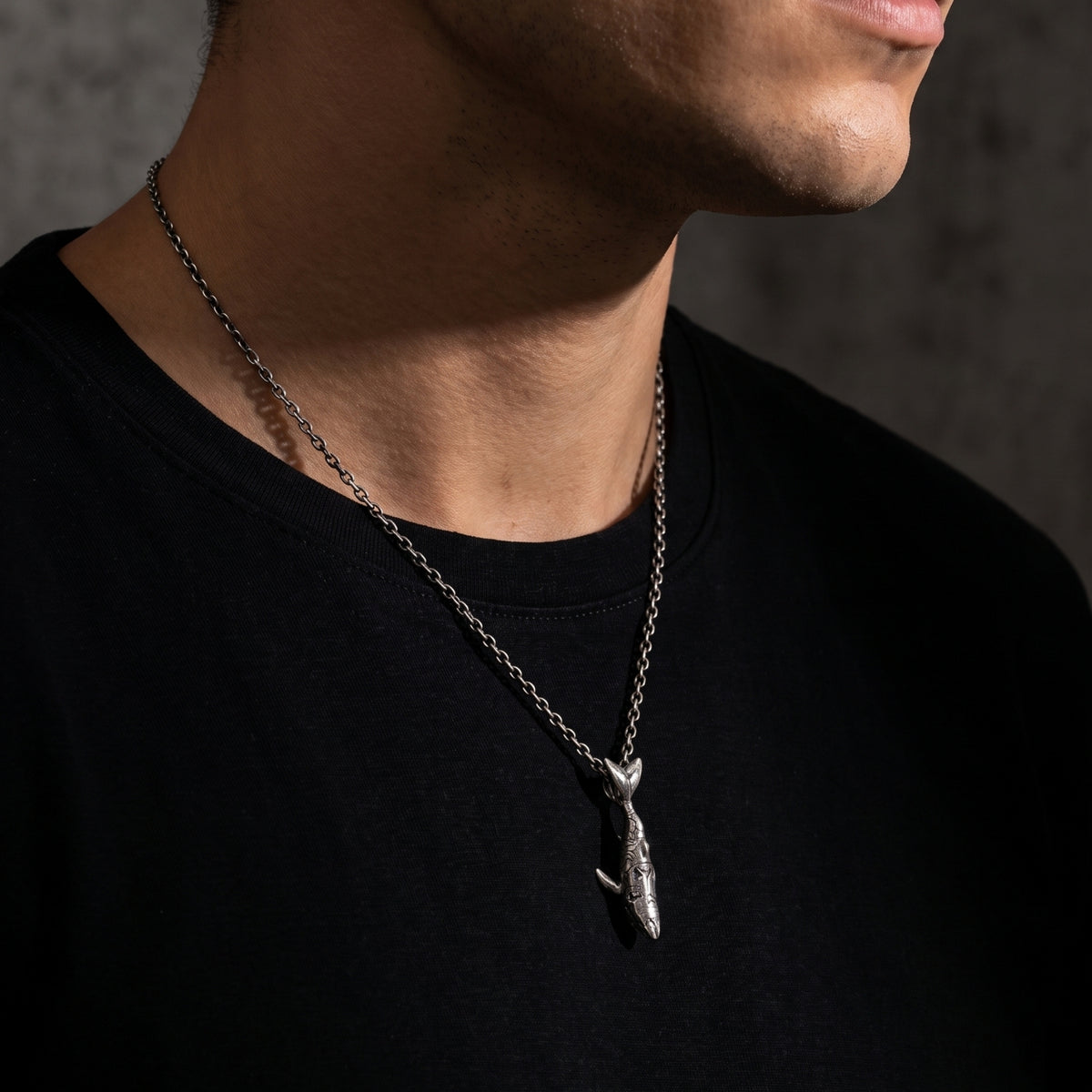 Side-profile view of a man wearing the oxidized silver shark pendant necklace over a black T-shirt.