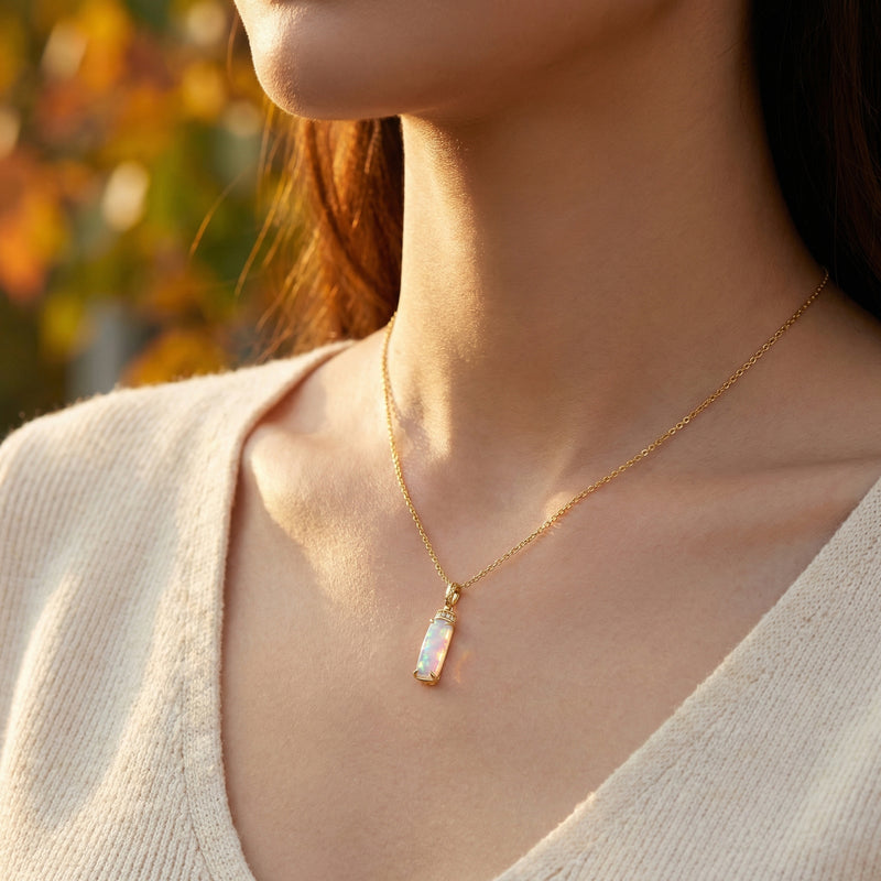Model wearing the gold-tone Galatea column necklace with a natural white opal pendant against an outdoor background.