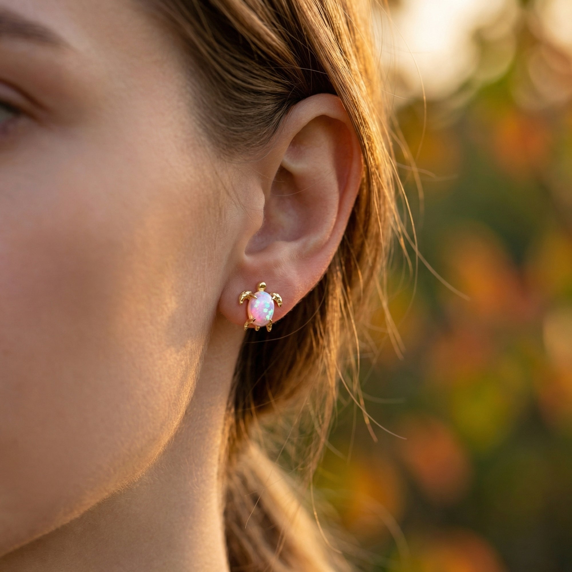 Gold-tone turtle earring with an oval white opal worn on a woman's ear in soft outdoor light.