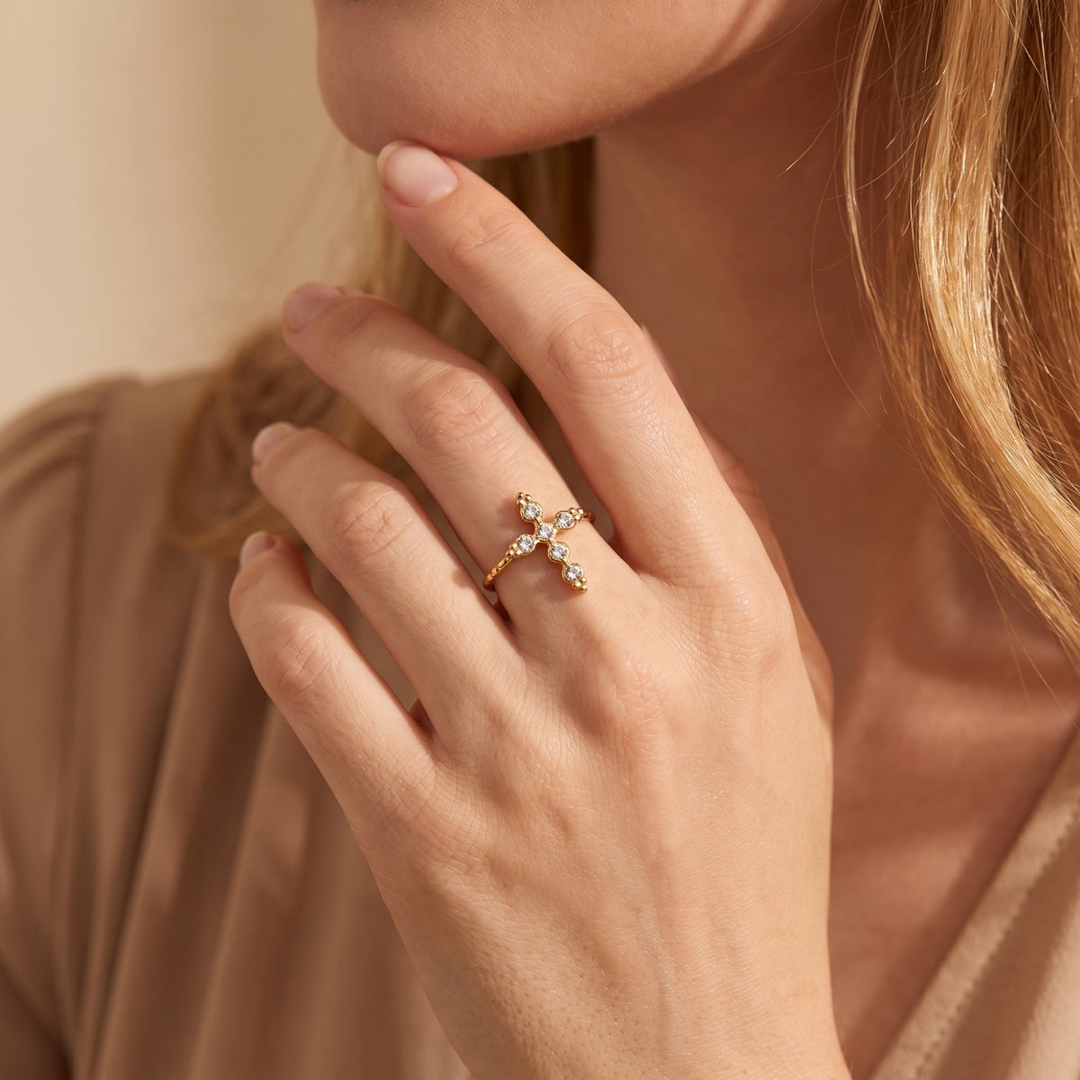 Model wearing the gold-tone crystal cross ring on her middle finger with her hand raised near her chin.
