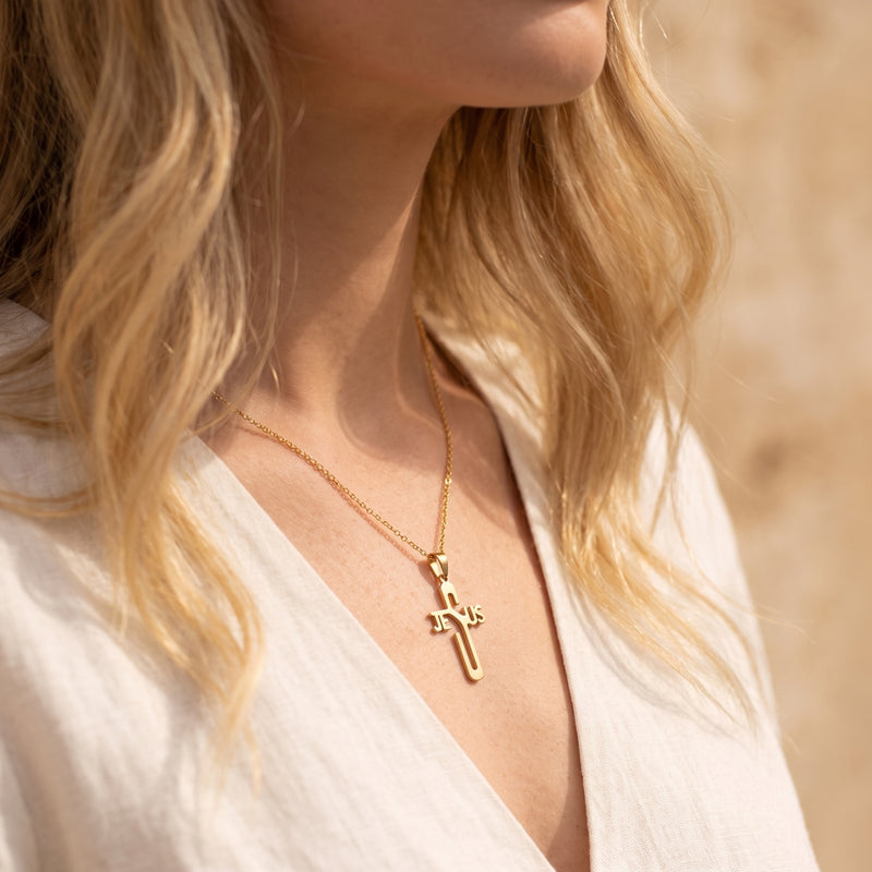 Woman wearing a gold-tone Jesus cross necklace over a white top.