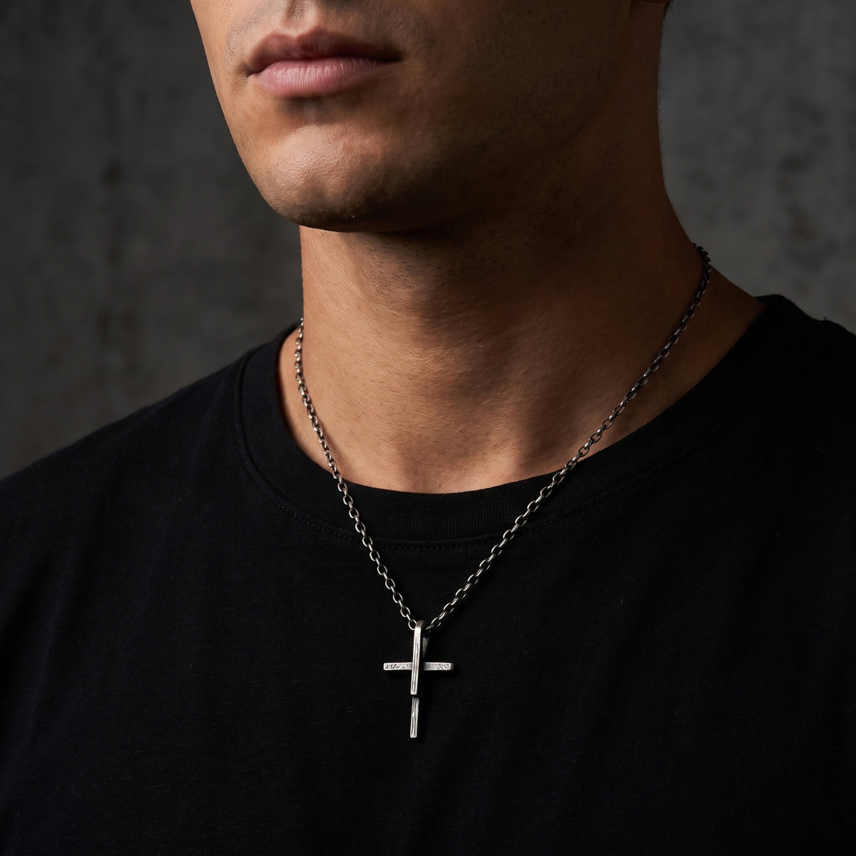 Textured silver cross necklace worn around a man's neck over a black shirt.