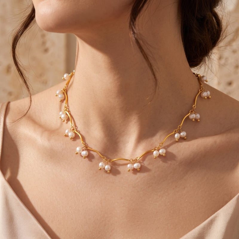 Close-up of the Aurendra gold finish wavy chain necklace with white drop pearls worn by a model.