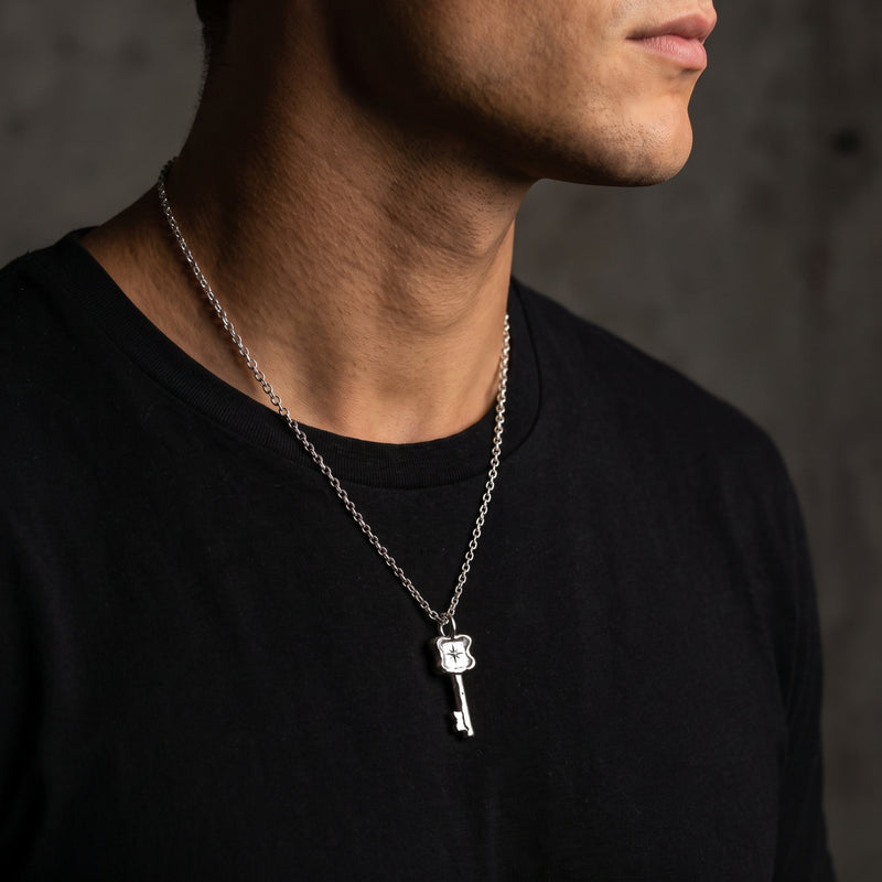 Side view of a man wearing a silver starburst key necklace over a black crewneck shirt.
