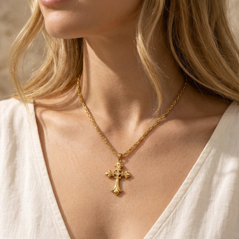 Model wearing an ornate gold-tone filigree cross necklace over a white V-neck top.