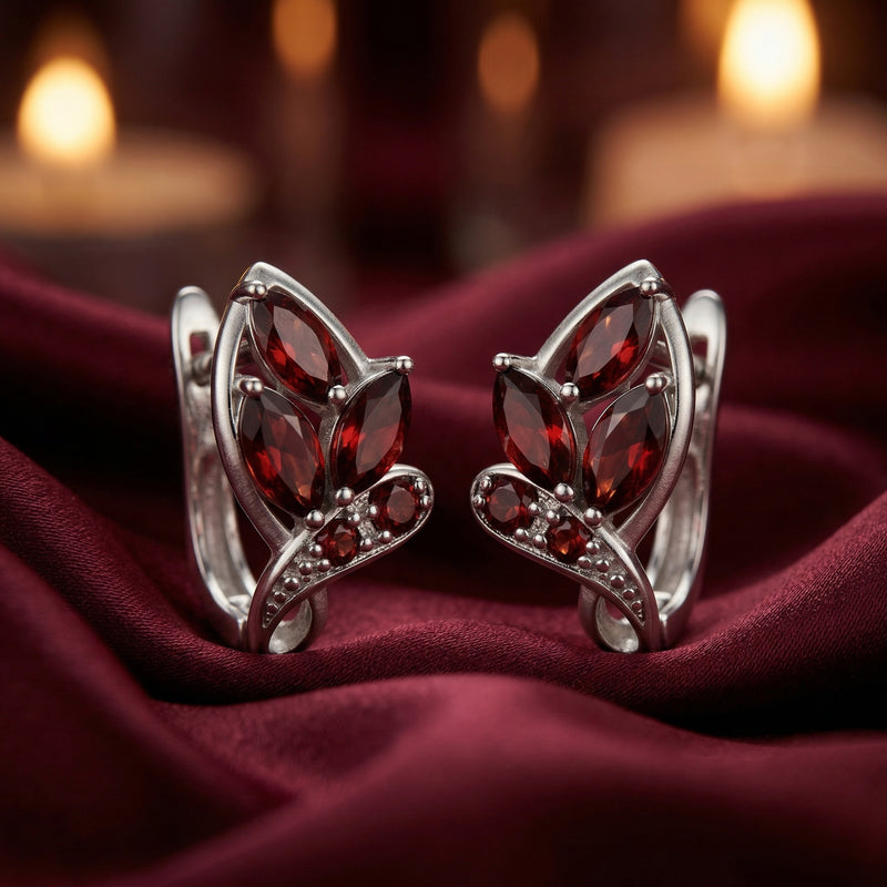 Front view of silver garnet drop earrings with marquise-cut stones on a draped red fabric.