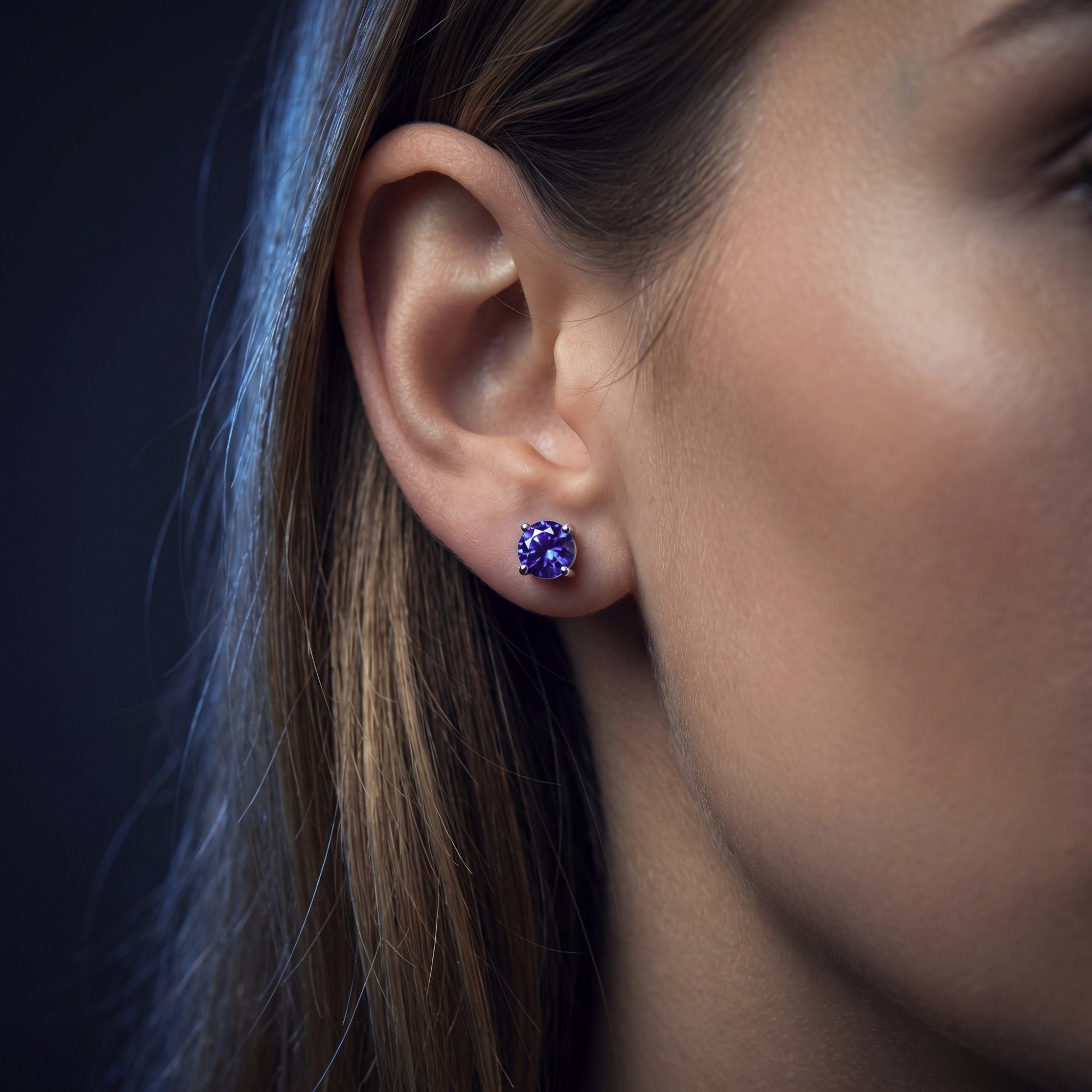 Woman wearing a violet-hued round cut tanzanite solitaire stud earring in 18K white gold.
