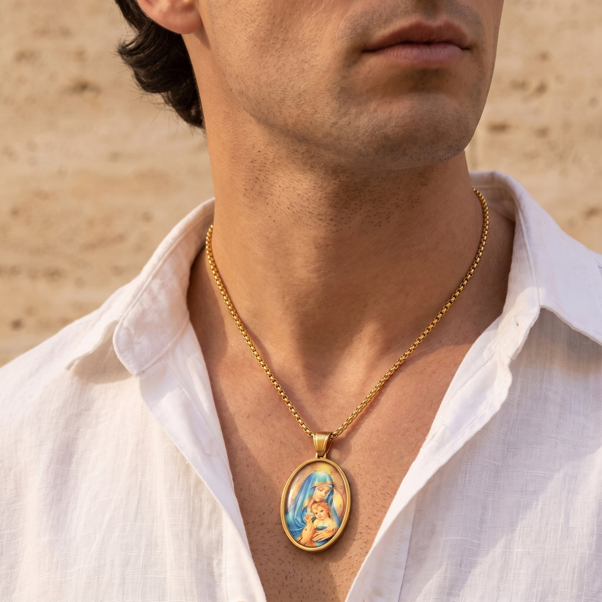 Male model wearing the gold-tone Madonna and Child oval pendant necklace with an open white shirt.