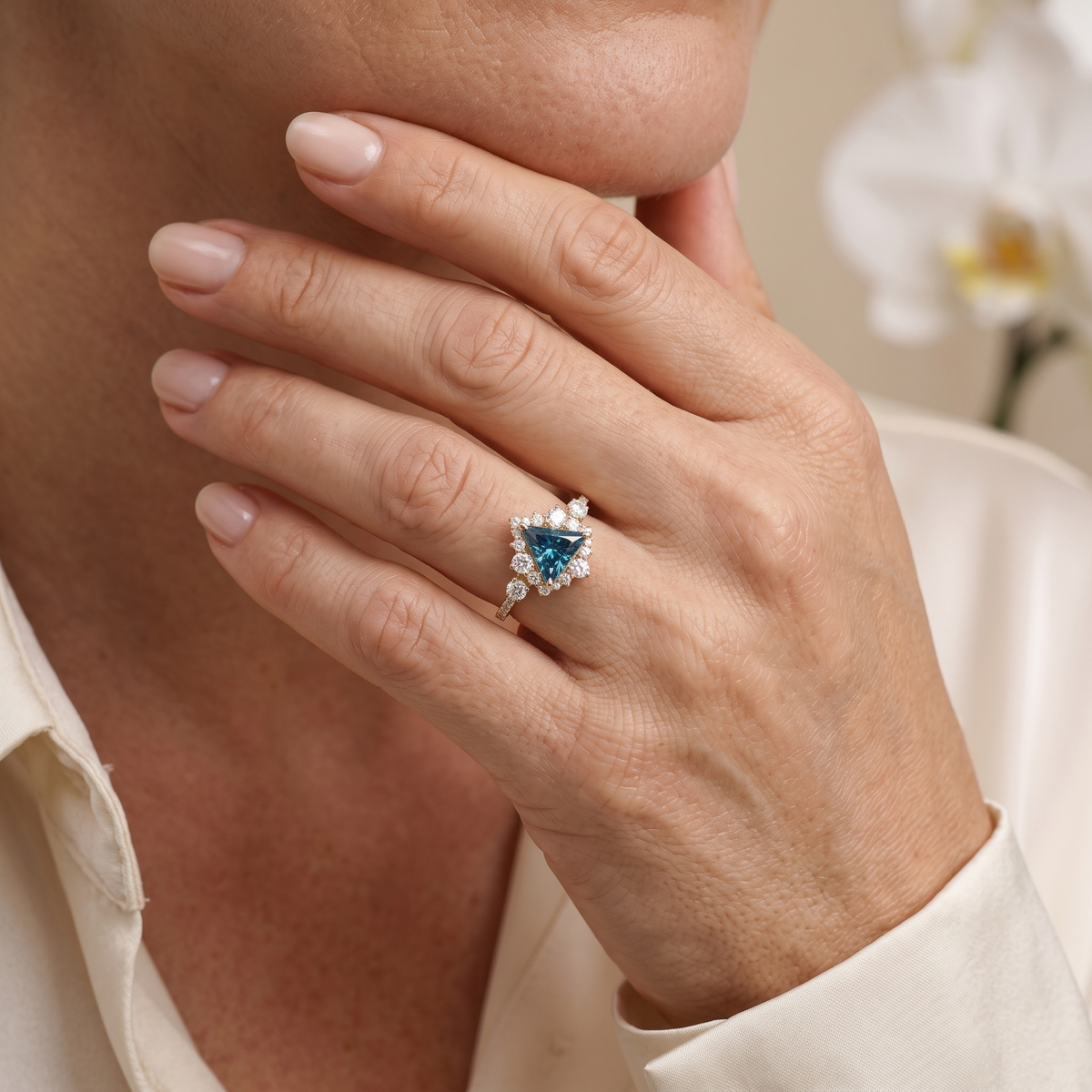 Rose gold triangle cut blue gemstone ring with diamond halo worn on model's hand.