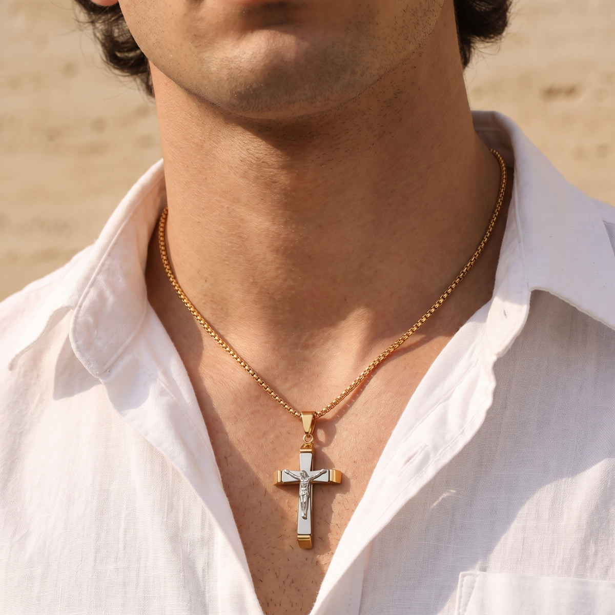 Front view of a person wearing the gold-tone chain and layered crucifix pendant over an open white shirt.
