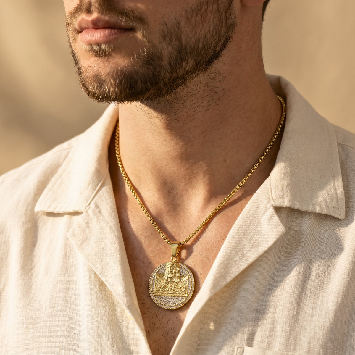 Close-up of a man wearing the gold-tone Last Supper medallion necklace with an open cream shirt.