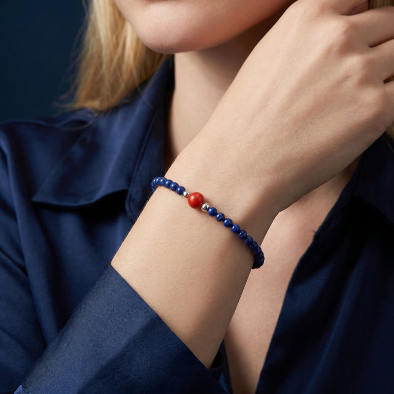 The Azure Trace round lapis bead bracelet with a red center stone worn on a woman's wrist with a blue silk shirt.