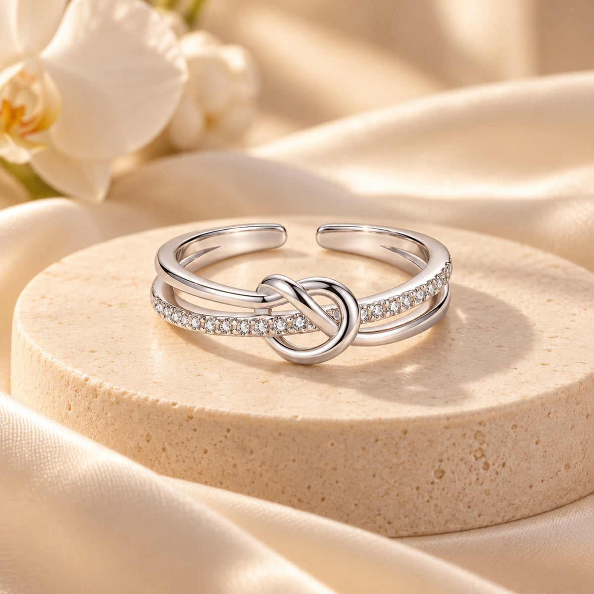 Silver S925 open-back heart and infinity knot ring with clear stone accents on a cream pedestal
