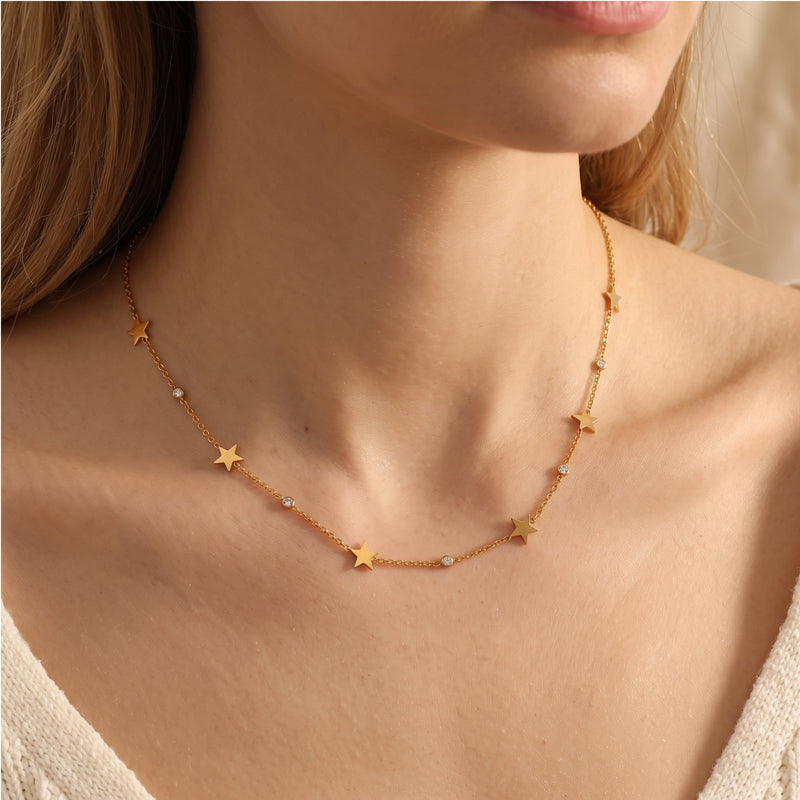 Gold star charm necklace with simulated diamond bezels worn on a woman's collarbone.