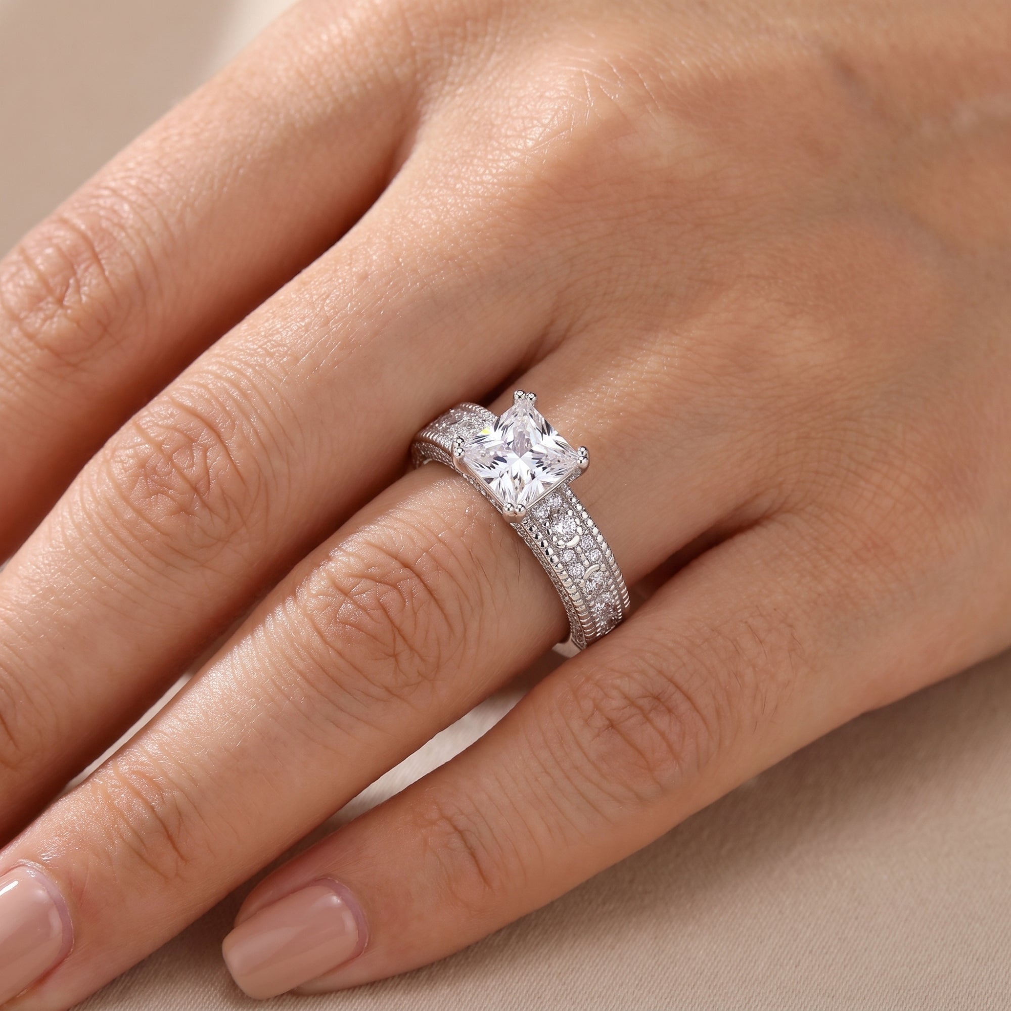 Close-up of princess cut CZ silver ring on a finger.