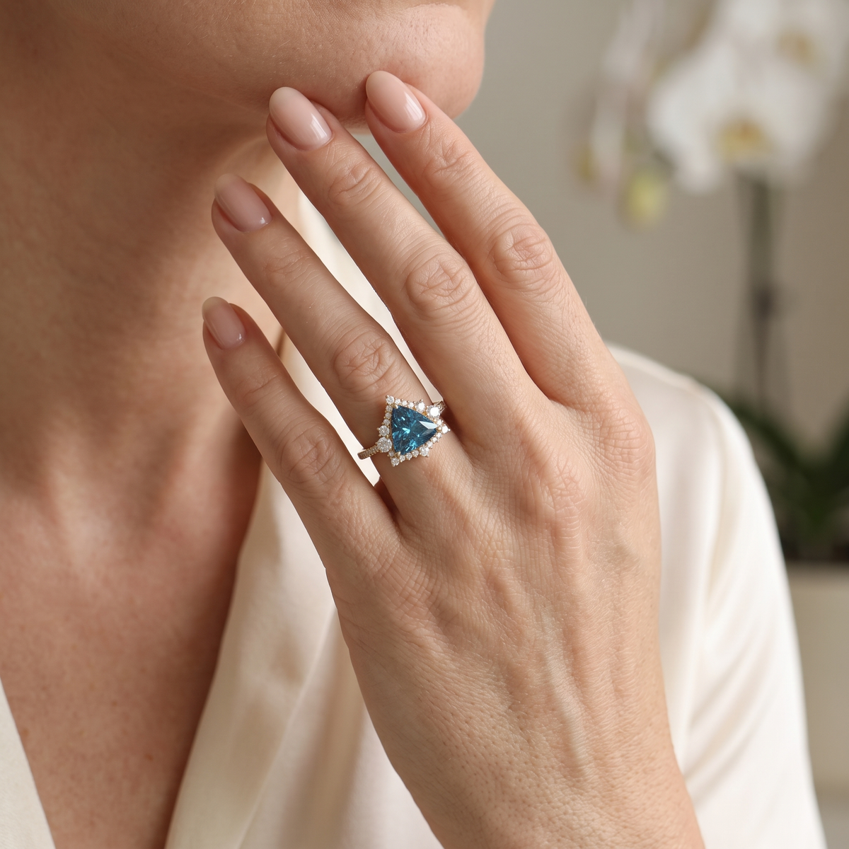 Trillion-cut blue moissanite halo engagement ring in rose gold worn on a hand.