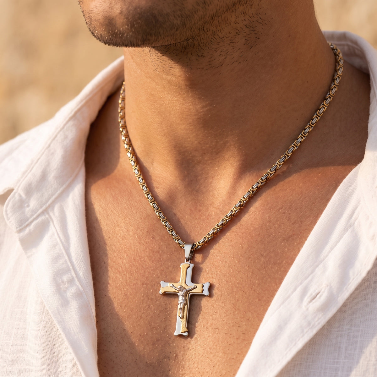 Close-up of a man's neck and chest wearing a two-tone crucifix pendant on a Byzantine chain.