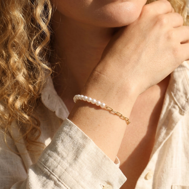 Woman wearing the gold and pearl Lenora bracelet on her wrist, paired with a linen shirt.