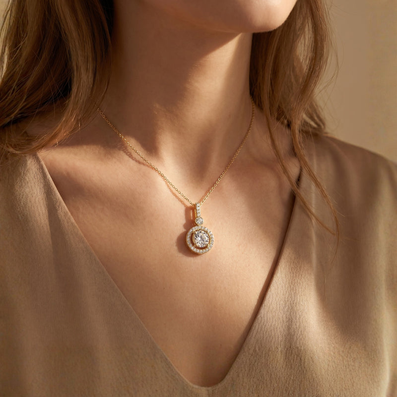 Woman wearing the gold Antoinette moissanite halo pendant necklace with a round cut center stone.