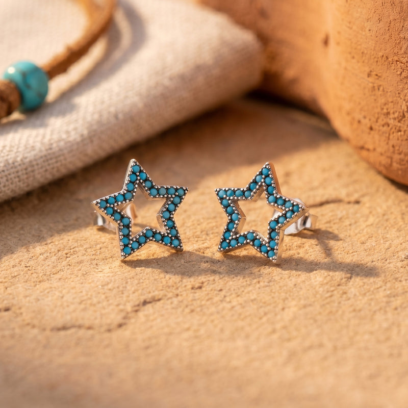 Pair of sterling silver star stud earrings with turquoise pave stones displayed on a textured stone surface.