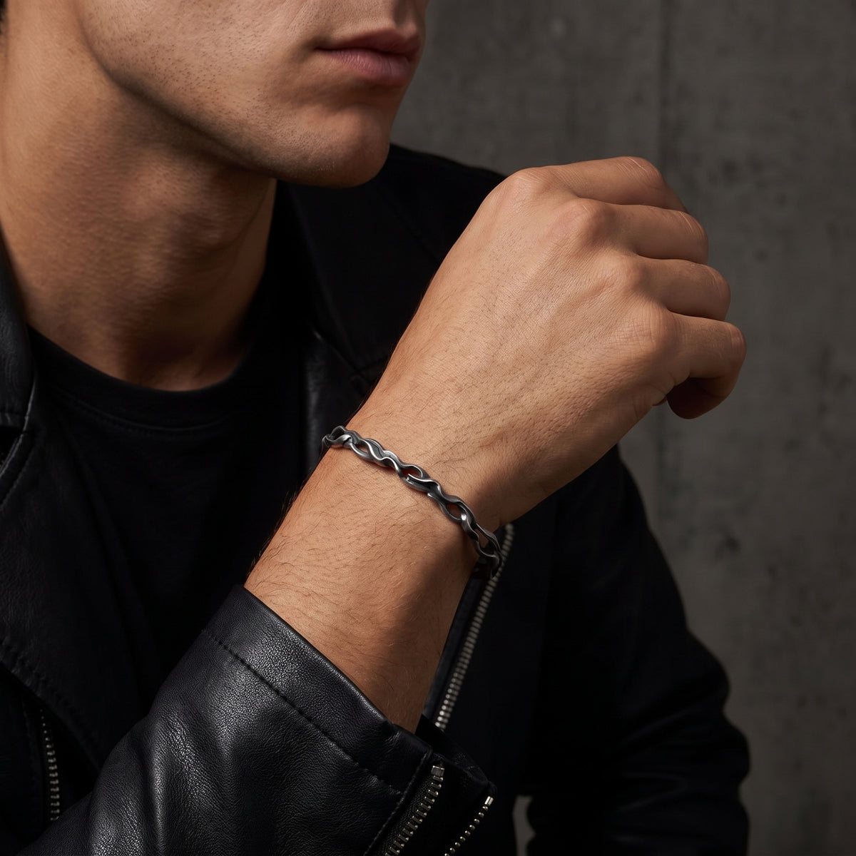 Model wearing a silver wave cuff bracelet with a black leather jacket, hand raised near his chest.